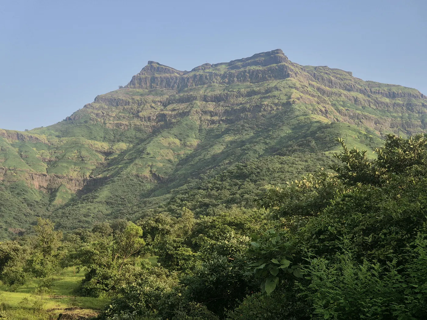 Torna Fort's long ridgeline rising above green, wooded slopes on a clear morning