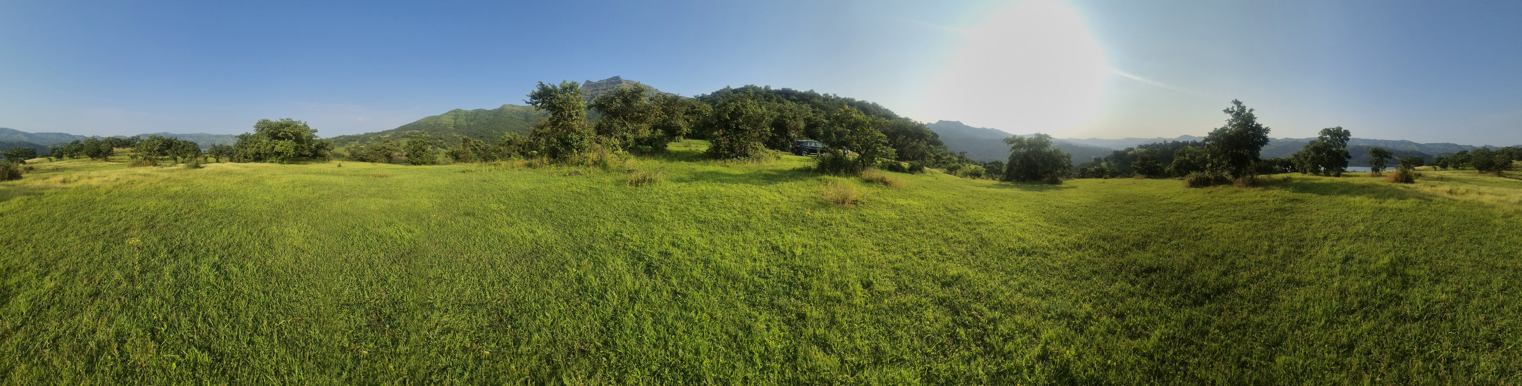 Panoramic view across open green project land, trees and the Sahyadri mountain ridges near Velhe