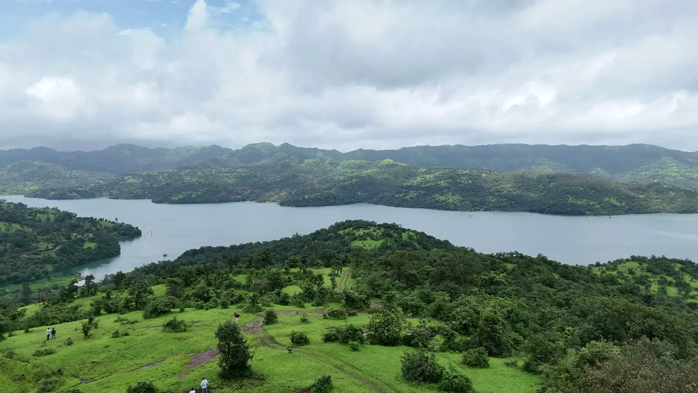 Green meadows sloping down to wide backwaters, with forested ridges and monsoon clouds beyond