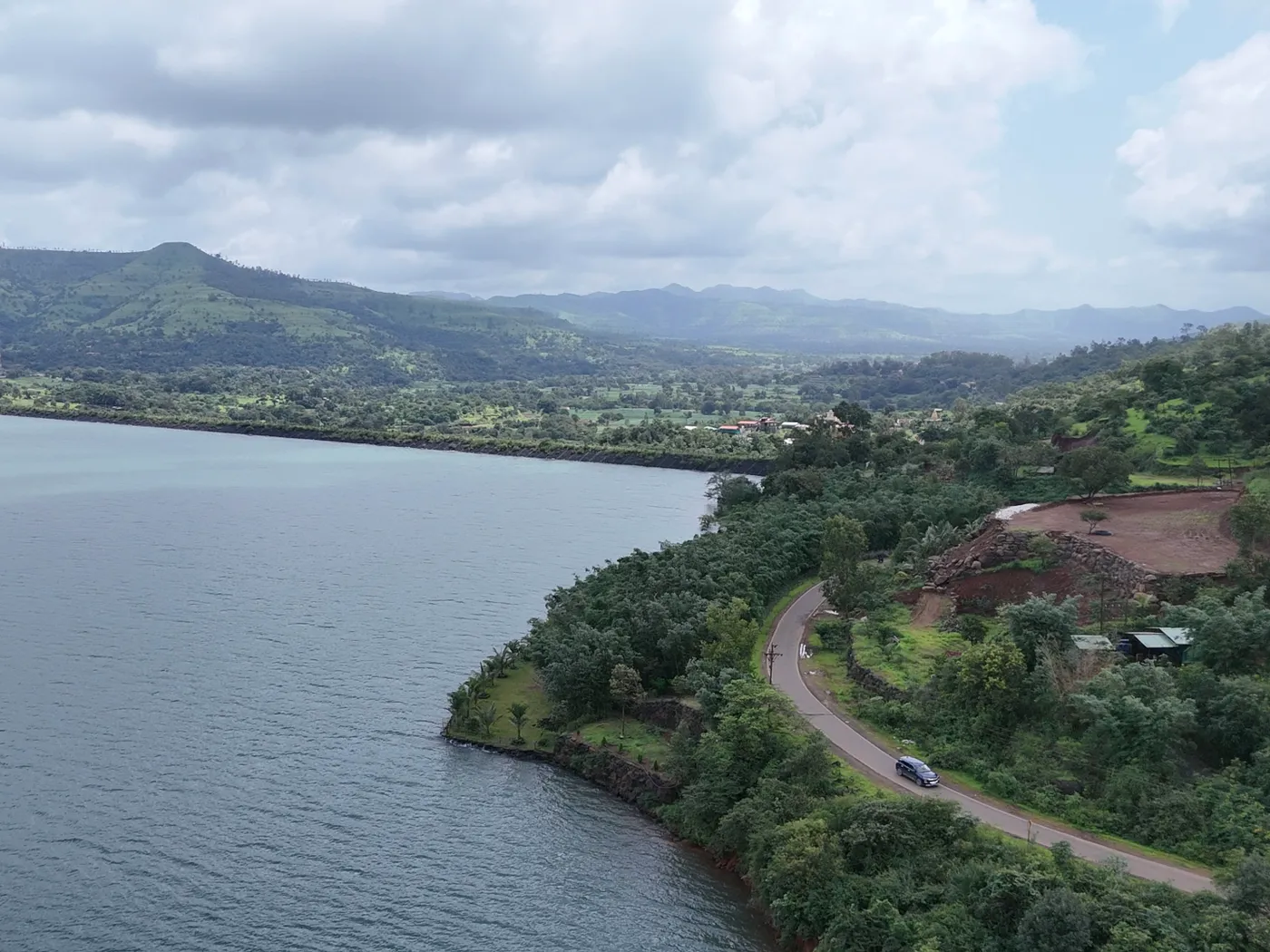 A car on the road curving along the backwaters below green hills